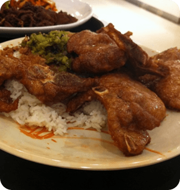 A plate of fried pork over rice with greens, on a lunch-counter table.