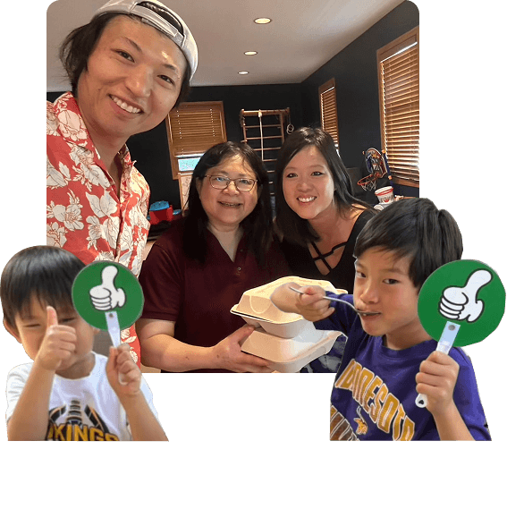 The Two Sons family in their kitchen, holding a bian dang box, with two boys giving a thumbs up.